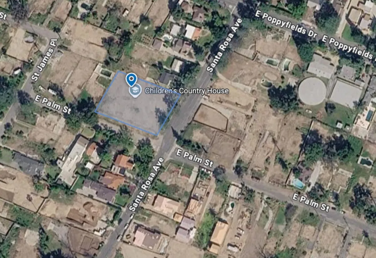 Aerial view of an Altadena neighborhood block with a vacant, fire-cleared lot outlined amid surviving tree canopy and rebuilding homes