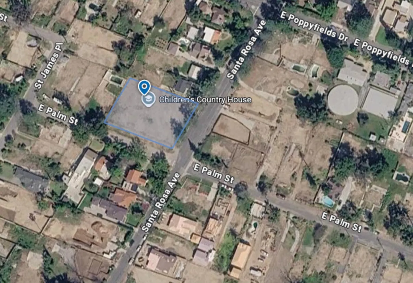 Aerial view of an Altadena neighborhood block with a vacant, fire-cleared lot outlined amid surviving tree canopy and rebuilding homes